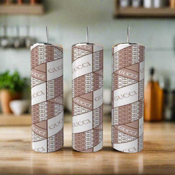 Three cylindrical tumblers featuring a pink "GUCCI" inspired pattern from Kreative Kreationz’s 20oz Tumbler Collection are arranged side by side on a kitchen counter, their stylish design standing out against the blurred background.