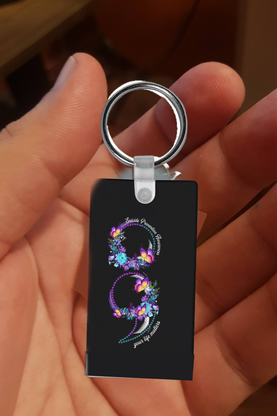 A person holds the Suicide Prevention Awareness Keychain by Kreative Kreationz—a black sublimation accessory featuring a colorful, floral dragon 