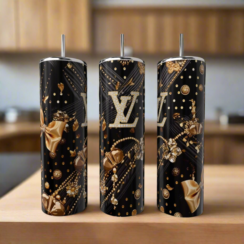 Three Louis Vuitton Black & Gold 20oz tumblers by Kreative Kreationz, featuring metallic gold and silver floral designs, bows, and the iconic LV logo, are displayed on a wooden surface in a modern kitchen.