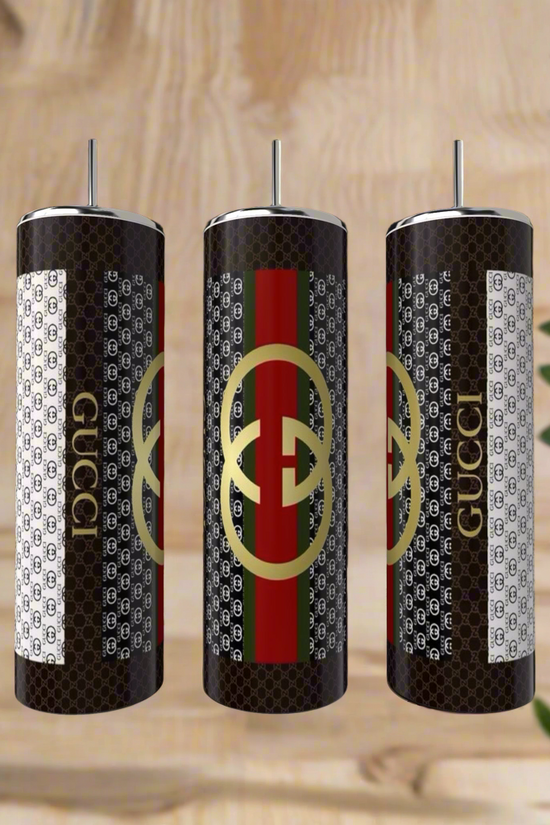 The Gucci 20oz Tumbler by Kreative Kreationz features luxury-inspired black-and-white patterns, metallic straws, and a gold logo with red and green stripes, all crafted from high-quality stainless steel for lasting style.