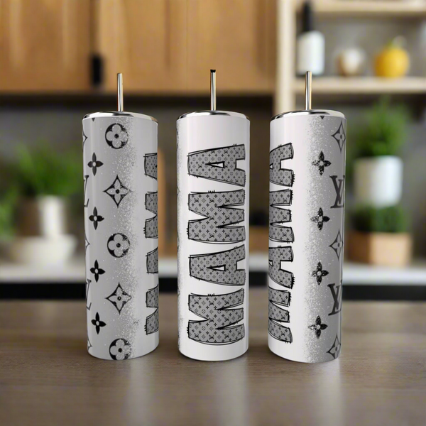 Three 20oz white cylindrical stainless steel tumblers from Kreative Kreationz, each with metal straws and unique designs, sit against a blurred kitchen backdrop. Two have luxury-inspired patterns, while the center tumbler reads "MAMA" in bold.