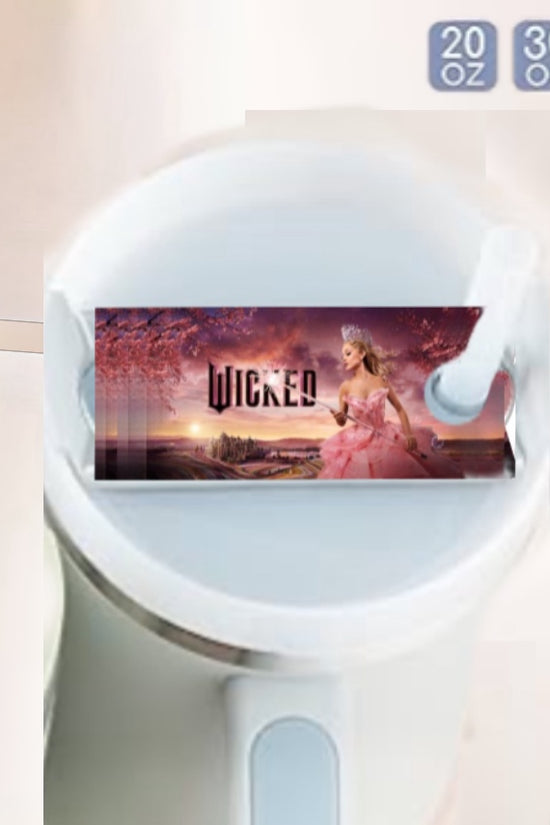 The white Stanley tumbler showcases a Wicked label with a woman in a pink gown and a landscape. Capacity indicators of 20, 30, and 40 oz are included in the upper right. Elevate your drinkware collection with the stylish Kreative Kreationz Wicked Stanley Lid Topper.