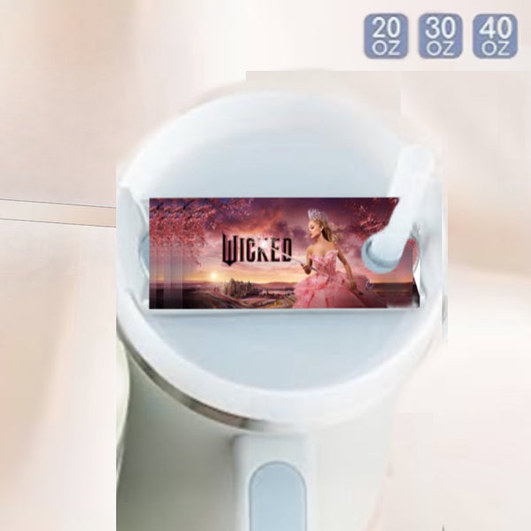 The white Stanley tumbler showcases a Wicked label with a woman in a pink gown and a landscape. Capacity indicators of 20, 30, and 40 oz are included in the upper right. Elevate your drinkware collection with the stylish Kreative Kreationz Wicked Stanley Lid Topper.