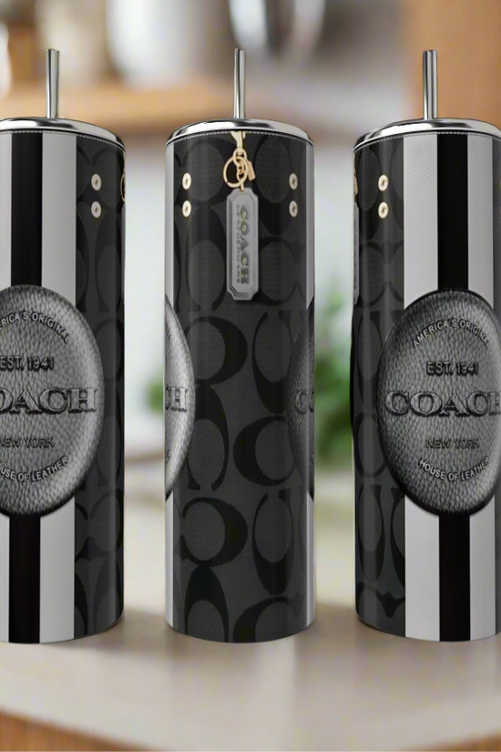Three black and silver Coach 20oz Tumblers by Kreative Kreationz stand on a kitchen counter, showcasing bold vertical stripes, a luxury look, and a circular Coach logo on the front.