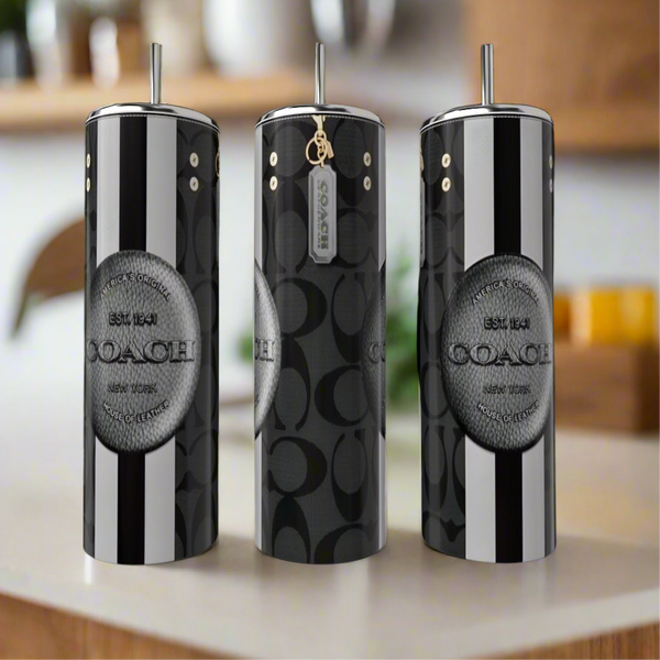 Three black and silver Coach 20oz Tumblers by Kreative Kreationz stand on a kitchen counter, showcasing bold vertical stripes, a luxury look, and a circular Coach logo on the front.