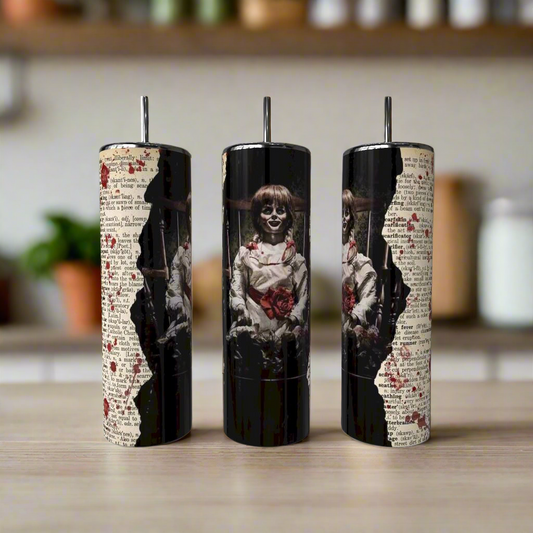 Three Annabelle 20oz Tumblers by Kreative Kreationz on a counter, each with torn vintage text and a creepy doll with glasses, solemn face, and red heart, set against a blurred kitchen background.