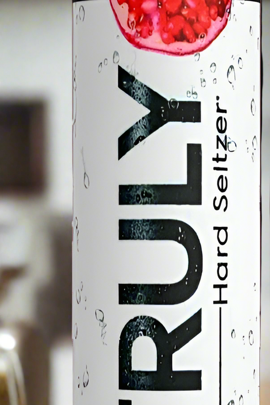 Four cans from the Truly Hard Seltzer 20oz Skinny Tumbler Collection by Kreative Kreationz are displayed on a wooden surface. The flavors showcased are pomegranate, passion fruit, pineapple, and another indistinguishable fruit. The sleek, tall cans feature refreshing water droplets on their design. Enhance your drinking experience with a reusable straw for an eco-friendly touch.