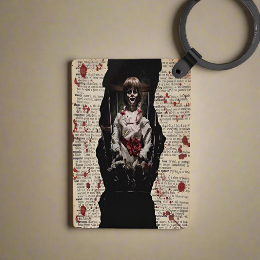 A notepad with red-stained pages and torn edges reveals a creepy doll image; nearby, a Kreative Kreationz Annabelle Inspired Keychain and a black magnifying glass rest on the desk.