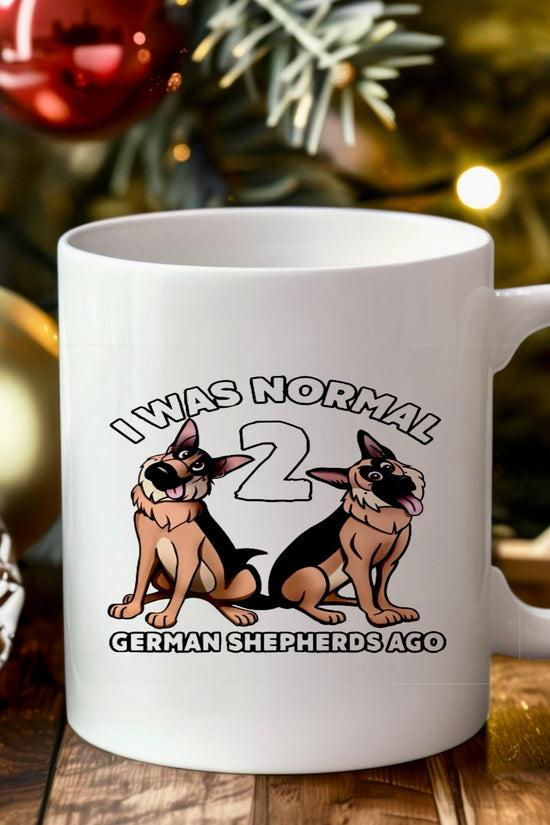 A white ceramic mug from Kreative Kreationz sits on a wooden table amid festive Christmas decor. Featuring two cartoon German Shepherds and the text, 