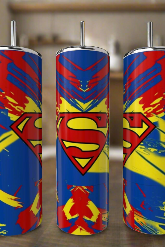 Three Superman Splash 20oz Tumblers by Kreative Kreationz, featuring bold red, blue, and yellow designs with the iconic “S” logo, stand on a kitchen counter—a vibrant eco-friendly drinkware set for fans.