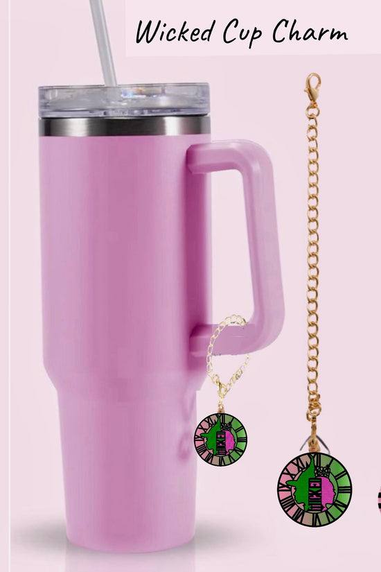 A pink tumbler with a clear lid and straw is shown next to the Kreative Kreationz Wicked l Charm Dangle, featuring a green and purple design with a witch hat motif on a gold lobster clasp chain.