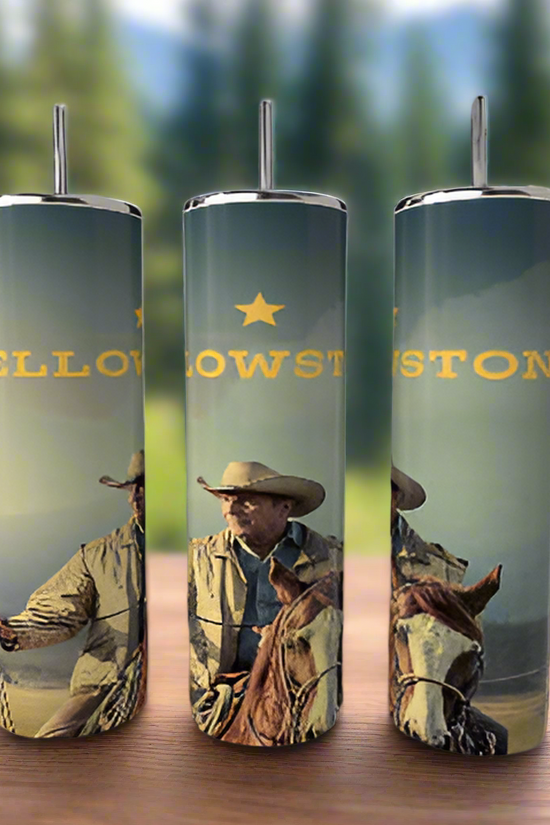 Three Kreative Kreationz Yellowstone 20oz Tumblers sit on a wooden surface, featuring cowboy and horse graphics with bold yellow text. The stainless steel tumblers are set against a blurred forest and mountain backdrop.