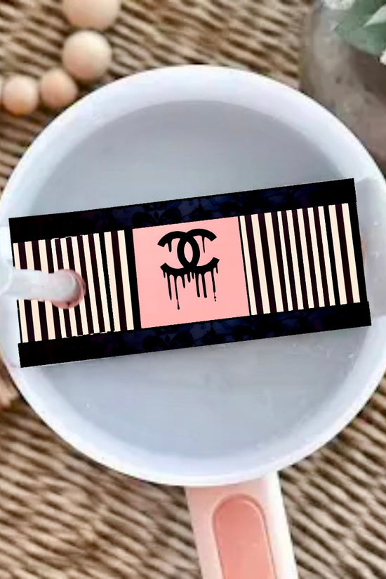 A round white cup with a pink handle sits on a woven surface, topped with the Chanel | Stanley Lid Plate/Topper by Kreative Kreationz, featuring beaded and floral accents—perfect for styling your Stanley tumbler.
