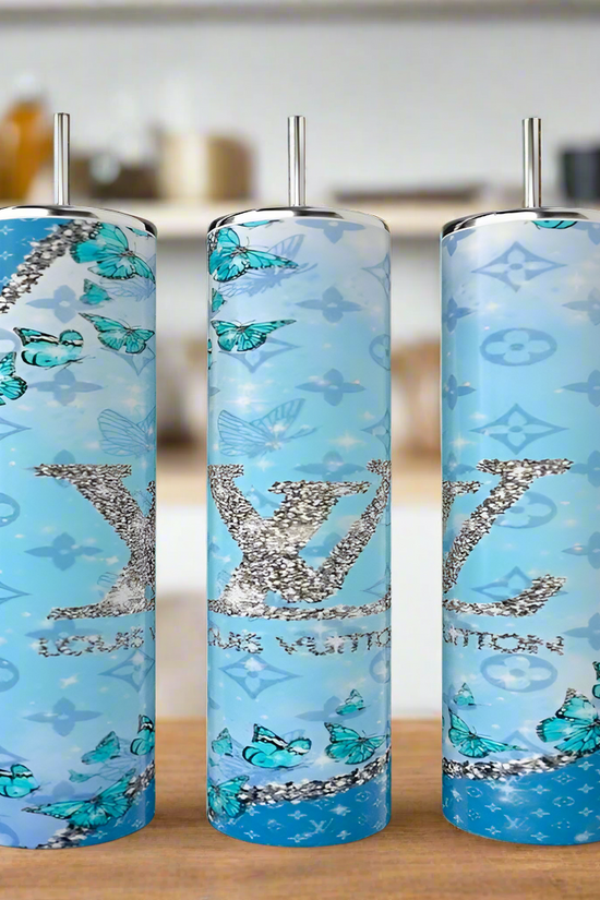 Three Kreative Kreationz Butterfly LV 20oz Tumblers with metal straws are shown on wood. Each features a luxury-inspired blue gradient with glittery 