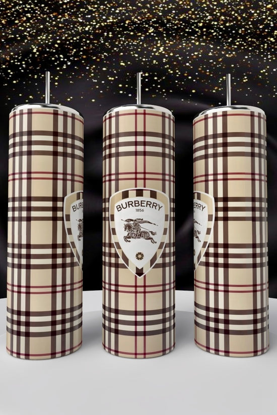 Three cylindrical Kreative Kreationz Burberry 20oz Skinny Tumblers, showcasing a signature plaid pattern and logo, stand on a white podium with golden sparkles against black satin—luxury drinkware elevated.