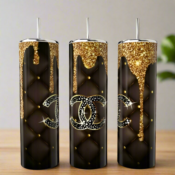 Three tall, black Chanel Gold Drip 20oz Tumblers by Kreative Kreationz feature quilted patterns, gold studs, glitter accents at the top, and a rhinestone double C logo, displayed on a wooden surface.