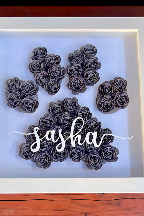 The Paw Print Shadow Box | Personalized by Kreative Kreationz features black paper roses forming a paw print on white, with your pet's name in elegant script on the glass—a unique and personal tribute.