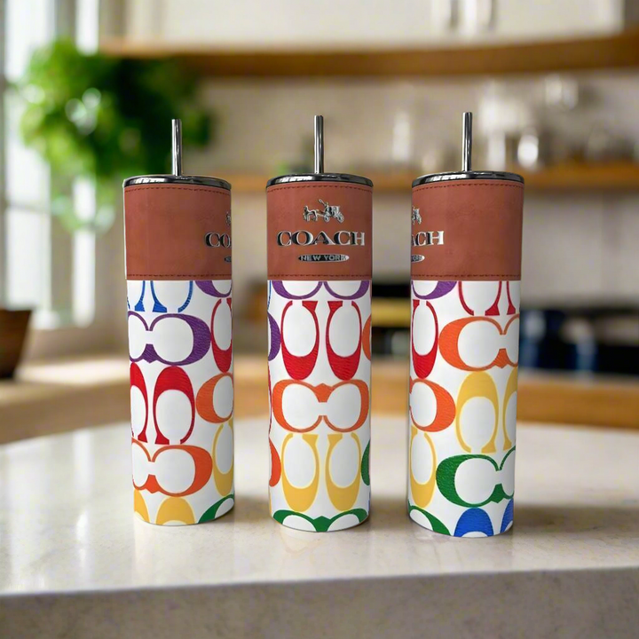 Three Rainbow Color 20oz Skinny Tumblers from Kreative Kreationz, featuring vibrant designs, stand on a kitchen counter with a blurred kitchen background.