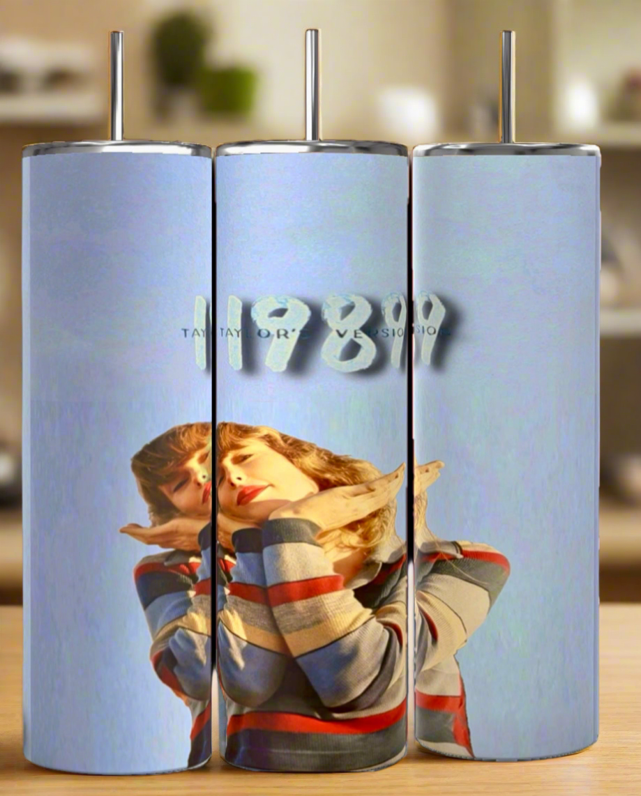 Three Kreative Kreationz Taylor Swift 1989 20oz tumblers with metal straws showcase a luxury blue design with a woman in stripes and "TAYLOR'S VERSION 1989" above her, displayed on a wooden surface.