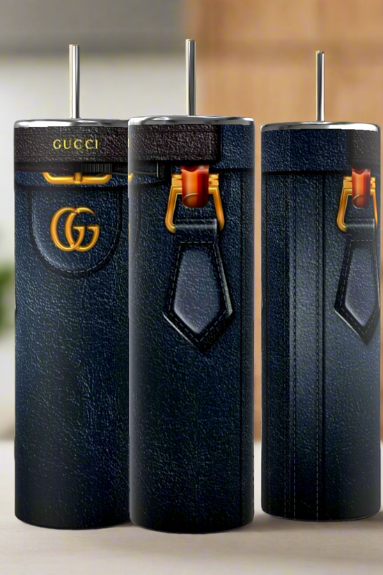 Three tall, blue leather-like Gucci Diana Purse 20oz Tumblers by Kreative Kreationz, adorned with gold accents, logos, vertical stitching, and red clasps, showcase their durable construction on a light surface against a blurred background.