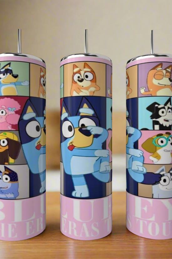 Three Bluey ERAS 20oz Stainless Steel Tumblers by Kreative Kreationz, featuring colorful show characters, are displayed on a wooden surface with a blurred kitchen background.