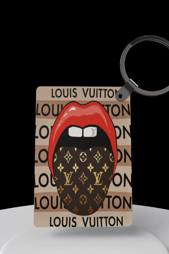 The LV Inspired Keychain by Kreative Kreationz features red lips with a tongue behind a Louis Vuitton-patterned mask on a beige 
