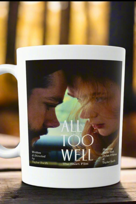 An All Too Well - Short Film Taylor Swift Ceramic Mug by Kreative Kreationz depicts two people gazing at each other and rests on a wooden surface against a blurred forest background.