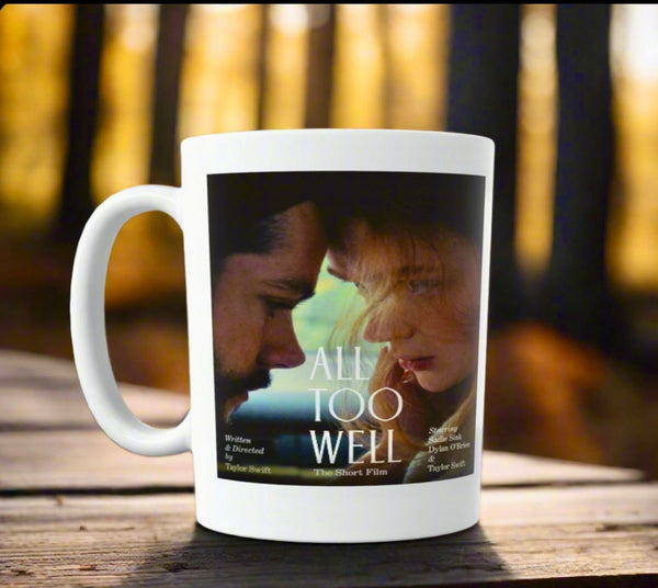 An All Too Well - Short Film Taylor Swift Ceramic Mug by Kreative Kreationz depicts two people gazing at each other and rests on a wooden surface against a blurred forest background.