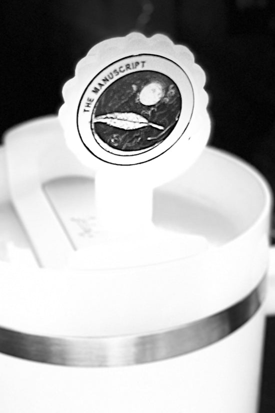 A white cup with a handle displays a round sticker on the lid, which features an illustration of a planet and spacecraft, accompanied by the text 