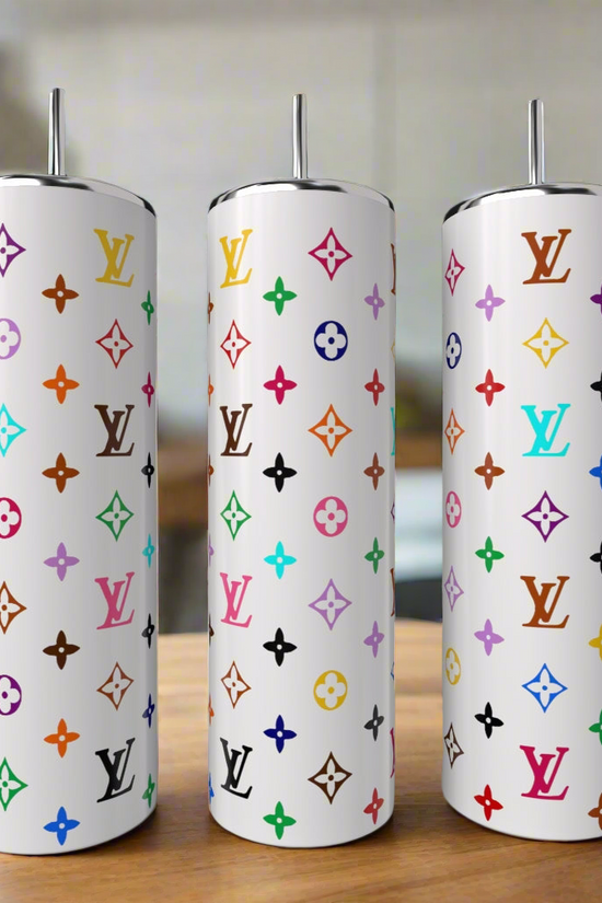 Three White LV Multicolor 20oz Tumblers by Kreative Kreationz, each with a metal straw and vibrant Louis Vuitton-inspired patterns, add luxury to your drinkware collection. Displayed on wood with a blurred kitchen in the background.