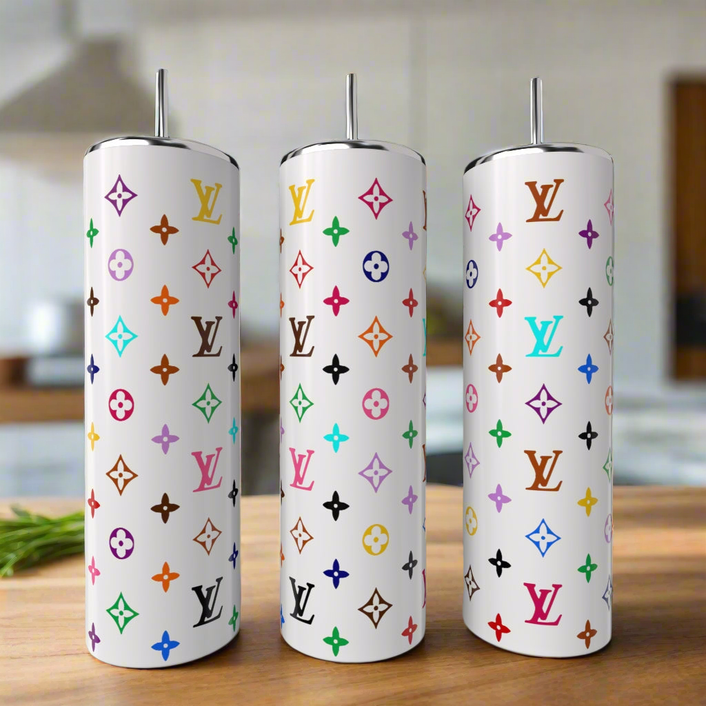 Three White LV Multicolor 20oz Tumblers by Kreative Kreationz, each with a metal straw and vibrant Louis Vuitton-inspired patterns, add luxury to your drinkware collection. Displayed on wood with a blurred kitchen in the background.