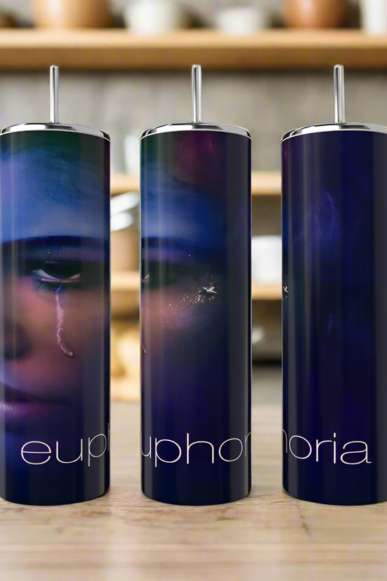 Three tall, dark blue Kreative Kreationz Euphoria Tumblers with stainless steel straws sit on a wooden surface. Each eco-friendly tumbler shows a close-up face with a tear and “euphoria” in white lowercase letters.