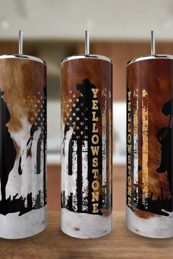 Three Kreative Kreationz Yellowstone 20oz Tumblers sit on a kitchen counter, each made of eco-friendly stainless steel and decorated with cowboy, bear, and horse silhouettes over a rustic American flag and cowhide design.