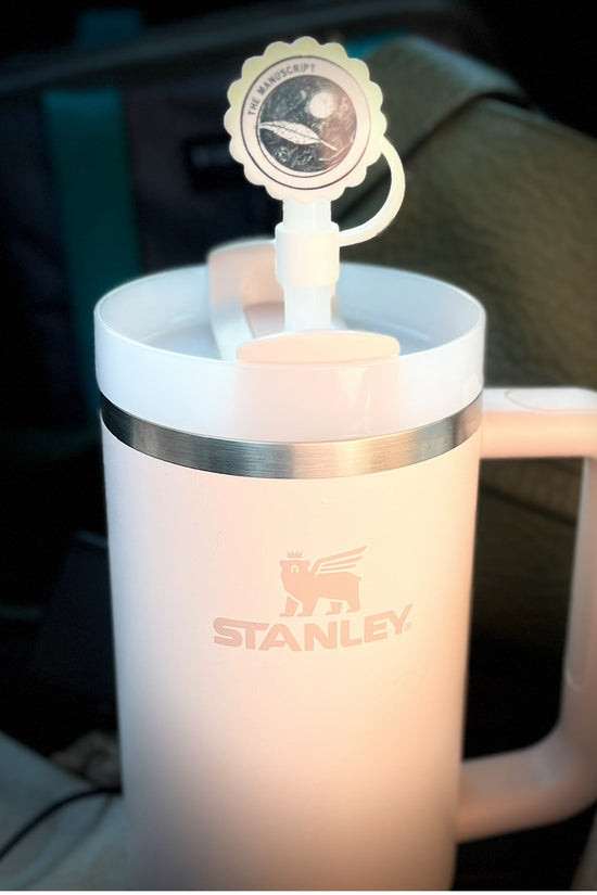 A white cup with a handle displays a round sticker on the lid, which features an illustration of a planet and spacecraft, accompanied by the text 