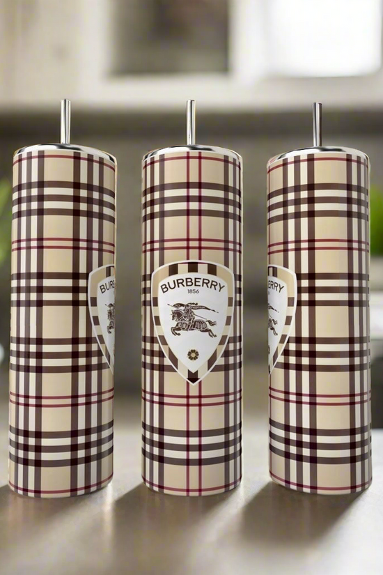 Three 20oz Skinny Tumblers by Kreative Kreationz, inspired by Burberry’s plaid, stand on a kitchen counter—stylish and elegant drinkware with blurred plant and stove in the background.