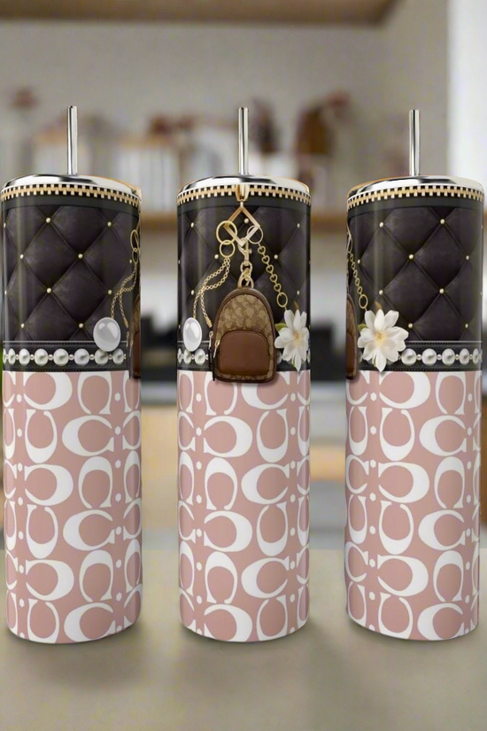 Three elegant Coach Lil Backpack 20oz Tumblers by Kreative Kreationz sit on the countertop. Each has a quilted black top and charming accent, with pink lower halves featuring white abstract designs, all made from eco-friendly, reusable materials against a blurred kitchen backdrop.