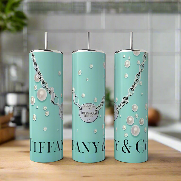 Three turquoise Kreative Kreationz Tiffany 20oz Skinny Tumblers with silver straws and pearl-and-chain designs rest on a wooden surface, displaying the brand name—ideal for stylish, eco-friendly drinkware.