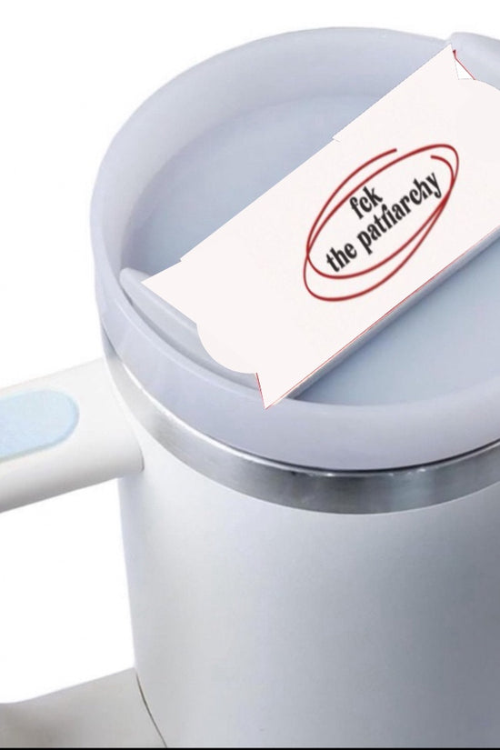 On a plain background sits a white mug adorned with the F#%k the Patriarchy Stanley Lid Plate/Topper from Kreative Kreationz. The topper features a piece of paper that boldly displays the text 