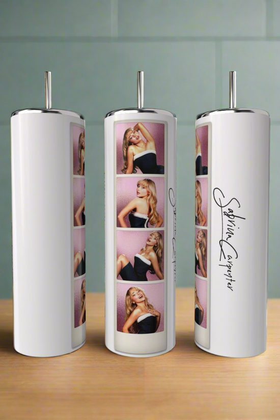 Three white Sabrina Carpenter Photo Strip Tumblers by Kreative Kreationz, each with a silver straw, eco-friendly design, and photo strip of Sabrina Carpenter posing against pink, plus her signature, are displayed on a wooden surface.