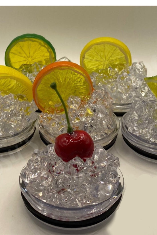 The Truly 20oz Tumbler from Kreative Kreationz, with its add-on 3D fruit and ice lid topper option, pairs perfectly with decorative coasters featuring realistic fake ice cubes. Each coaster is adorned with a different fruit slice or cherry—orange, lemon, lime slices, and a red cherry—arranged in a semi-circle on a white background.
