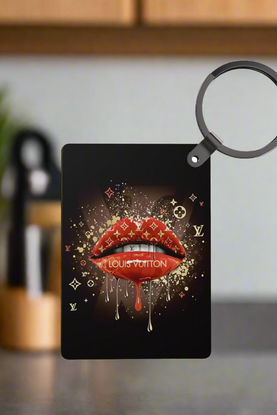 The Drip Lips LV Inspired Keychain by Kreative Kreationz features glossy red lips with gold drip and luxe accents, displayed in focus against a blurred kitchen backdrop.