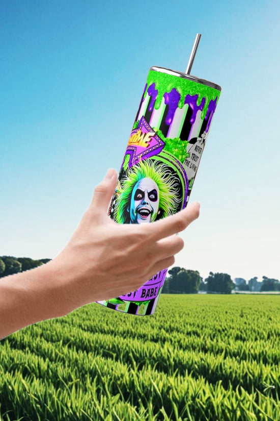 A hand holds a vibrant Beetlejuice Striped 20oz Tumbler by Kreative Kreationz, showcasing bold, bright colors and a cartoonish face with green hair set against a lush field. This Halloween drinkware comes with a straw for convenient sipping on the go.