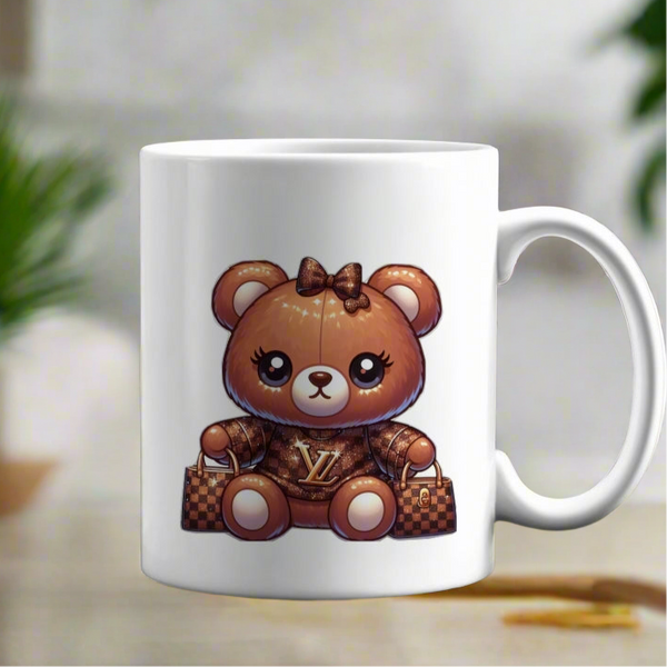 The Kreative Kreationz LV Bear 11oz Ceramic Mug features a cute cartoon teddy bear with a gold "LV" logo, brown outfit, bow, and designer-style bags on a softly blurred background. Dishwasher safe.