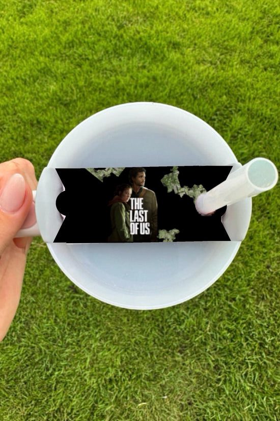 A hand holds a white cup with a straw and the Kreative Kreationz The Last Of Us Stanley Lid Topper, featuring 