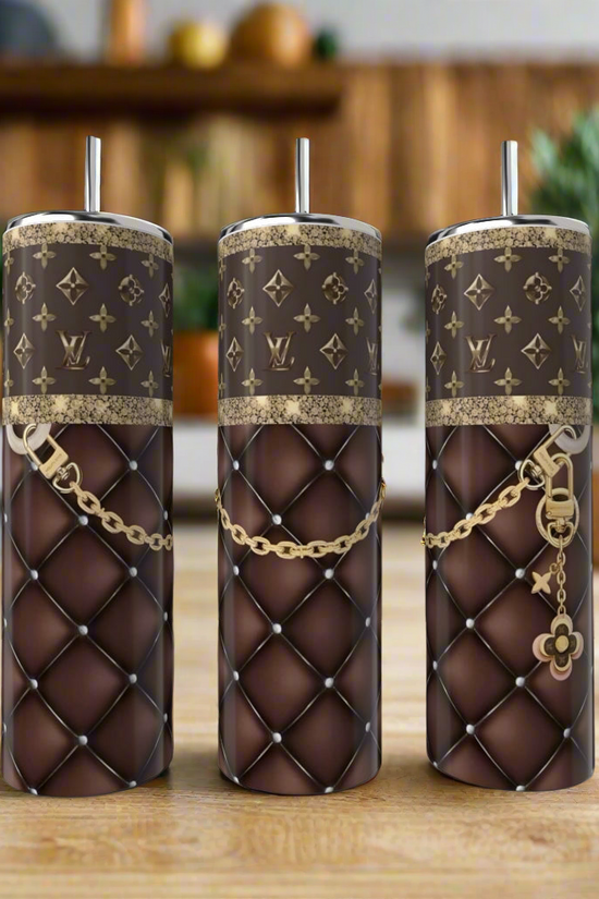 Three LV Purple & Gold 20oz Tumblers by Kreative Kreationz, featuring quilted brown leather-like patterns, gold chains, monogram designs, and metallic straws, bring a touch of elegance and luxury to your kitchen countertop.