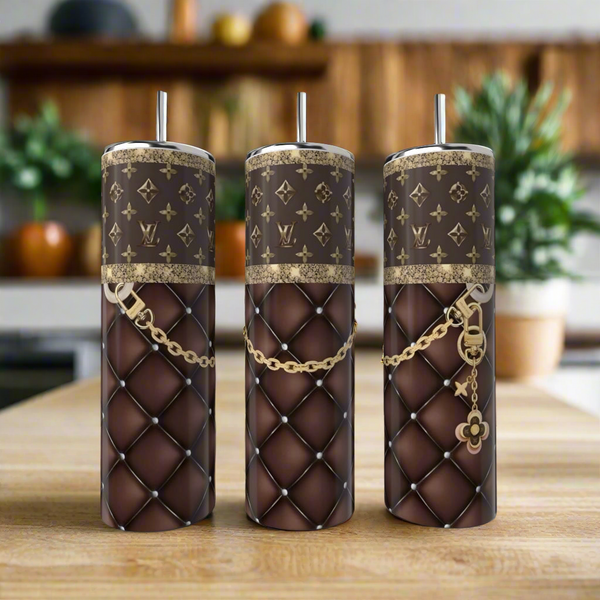 Three LV Purple & Gold 20oz Tumblers by Kreative Kreationz, featuring quilted brown leather-like patterns, gold chains, monogram designs, and metallic straws, bring a touch of elegance and luxury to your kitchen countertop.