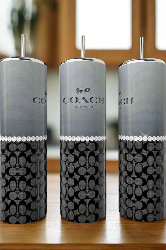 Three Coach Grey Black Pearl 20oz Skinny Tumblers by Kreative Kreationz, each with silver tops and straws, are displayed on a wooden surface. These stylish, reusable drinkware pieces are perfect eco-friendly options for your kitchen.