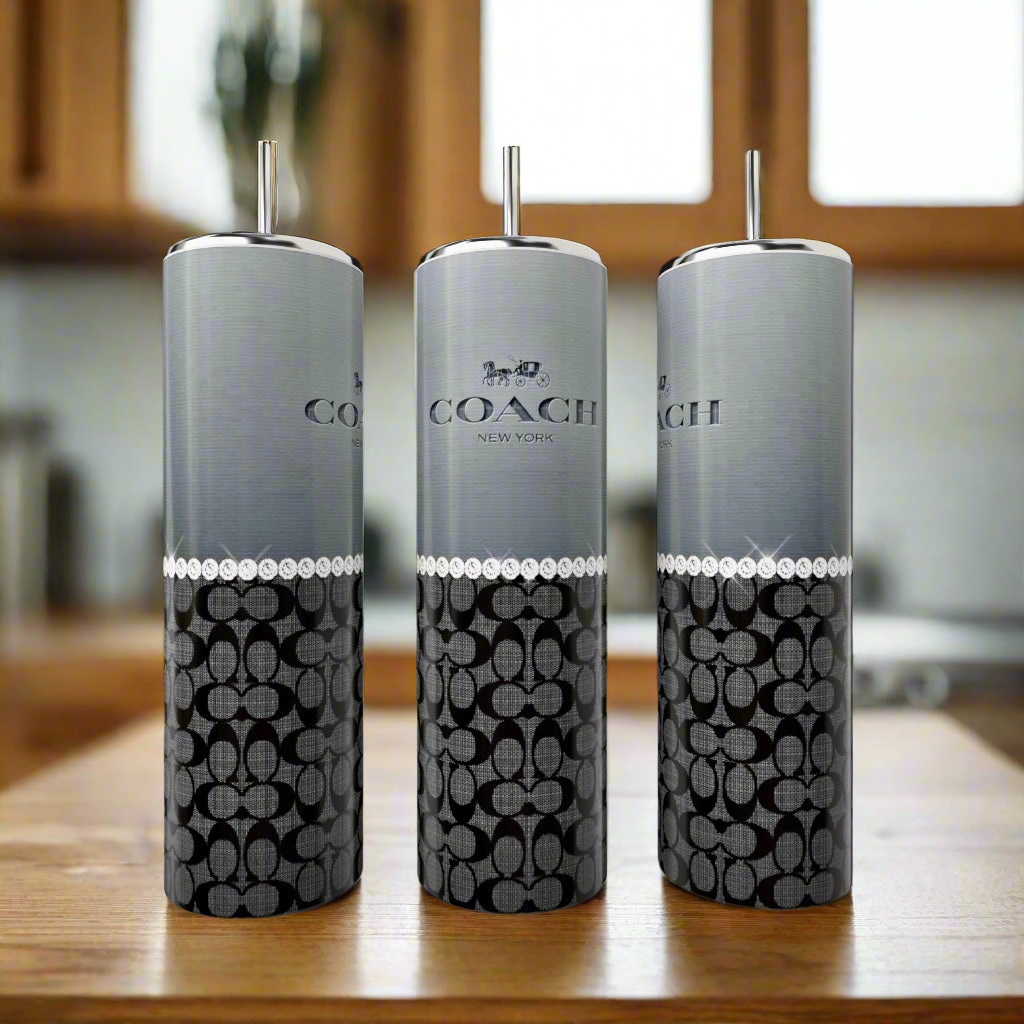 Three Coach Grey Black Pearl 20oz Skinny Tumblers by Kreative Kreationz, each with silver tops and straws, are displayed on a wooden surface. These stylish, reusable drinkware pieces are perfect eco-friendly options for your kitchen.