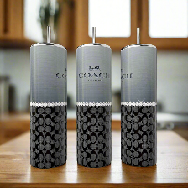 Three Coach Grey Black Pearl 20oz Skinny Tumblers by Kreative Kreationz, each with silver tops and straws, are displayed on a wooden surface. These stylish, reusable drinkware pieces are perfect eco-friendly options for your kitchen.