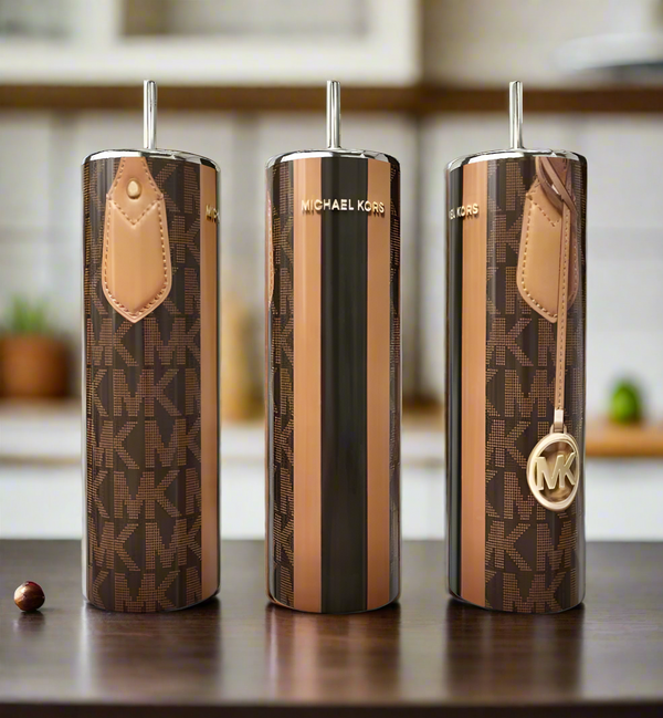 Three MK Strap 20oz Tumblers by Kreative Kreationz sit on a table, each featuring brown, tan, and gold designs with bold branding and metallic accents. All have straws and are shown against a blurred kitchen background.